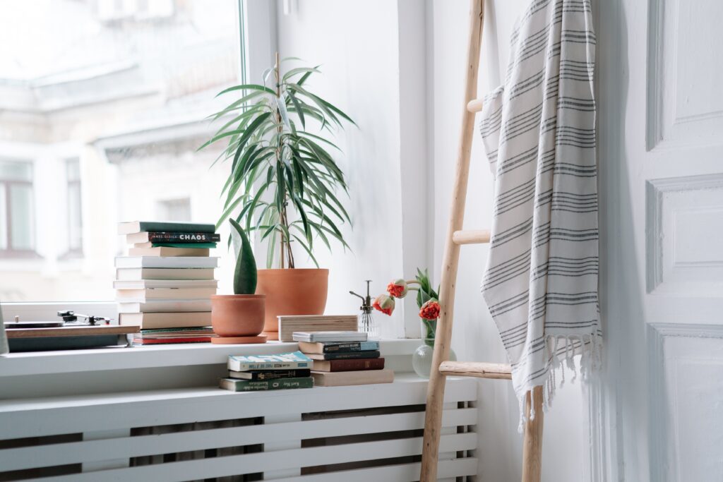 a radiator under an open window covered in books, plants, and a record player