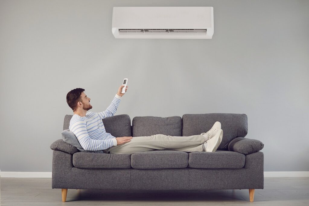 A man laying on a couch under a mini split heat pump air conditioner